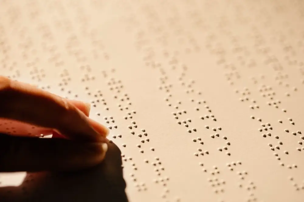 Close-up of a hand with fingertips resting on raised braille dots, reading a tactile page.
