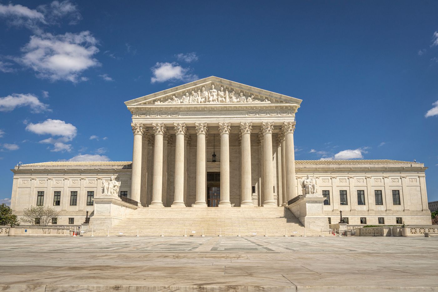 Front facade of the United States Supreme Court building in Washington, D.C., with tall marble columns and a wide staircase under a blue sky with scattered clouds.