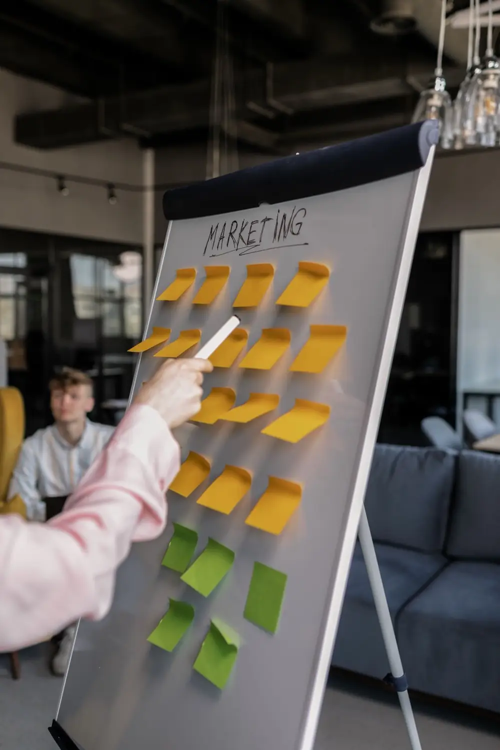 A person holding a pen points at a whiteboard covered with colorful sticky notes during a team planning session.