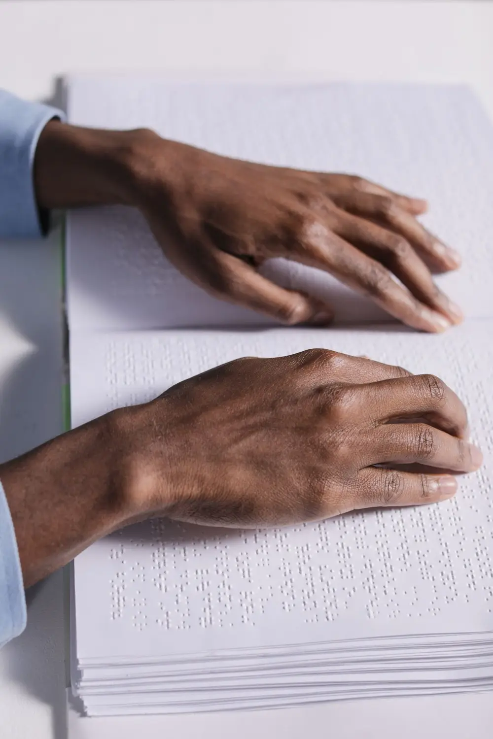 Close-up of a person's hands reading the raised braille dots across the open pages of a book.