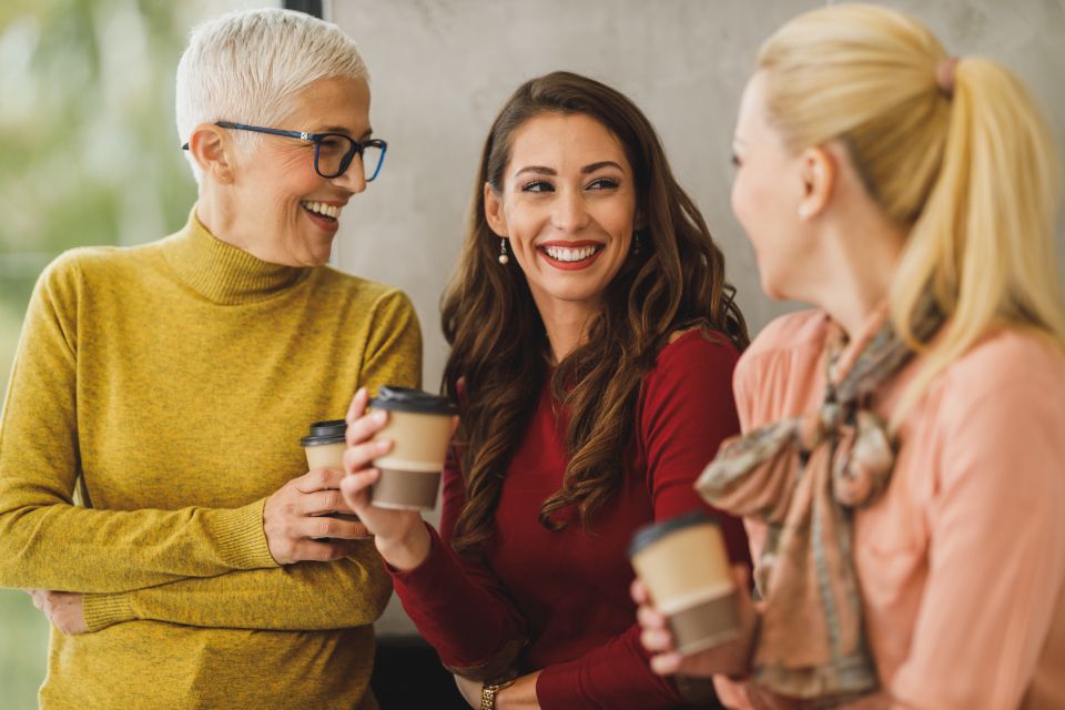 Three colleagues talking and laughing over coffee in an office